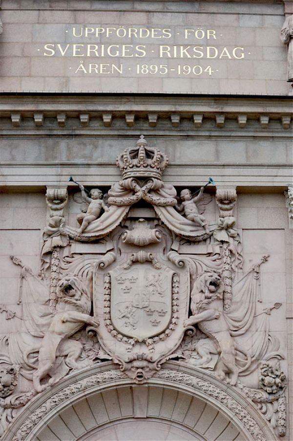 Скульптурная композиция над воротами Риксдага, изображающая герб страны, дополненный статуями львов, херувимов и короны – символа монаршей власти.